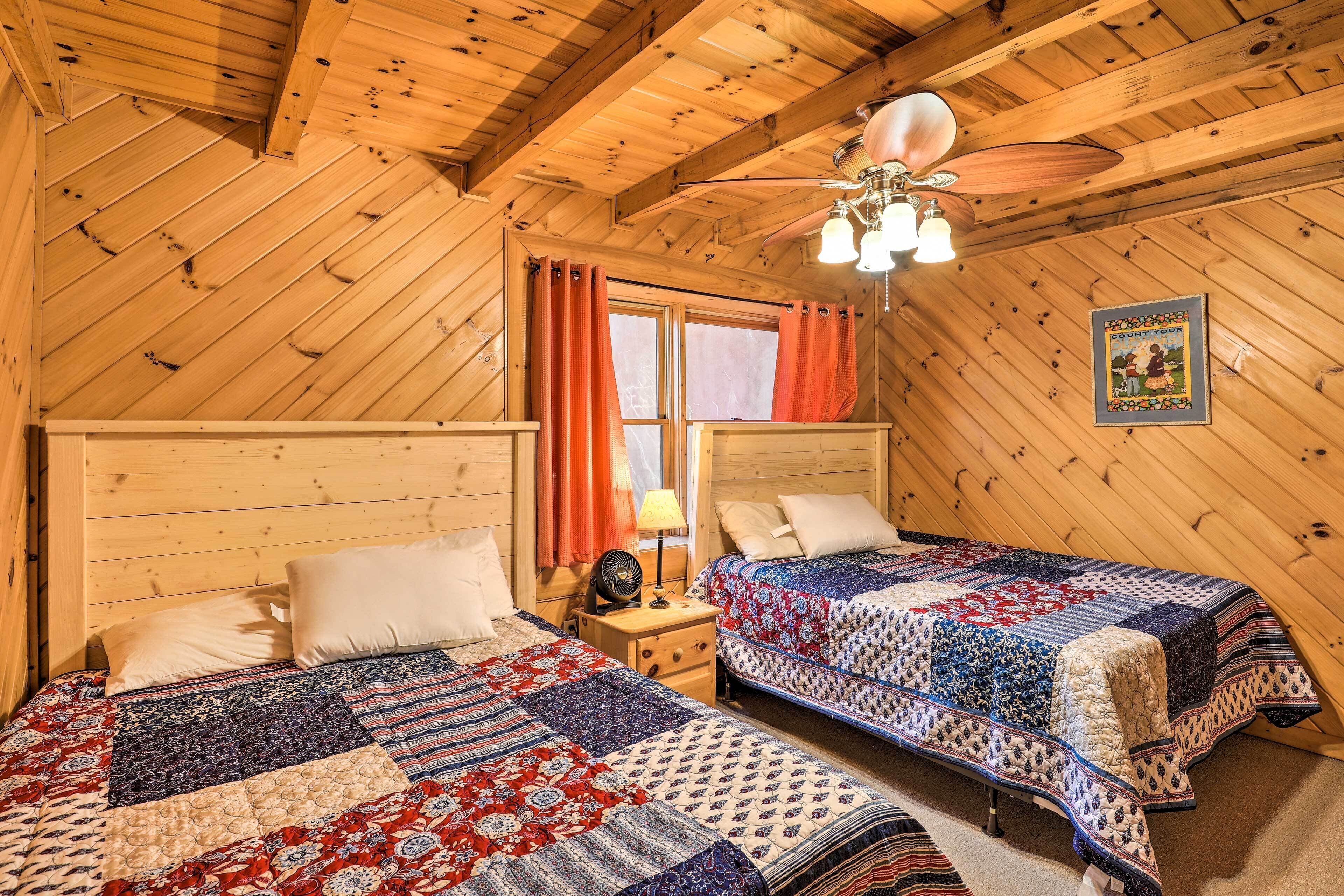 A cozy room with two beds, wooden walls, a ceiling fan, and a window with curtains.