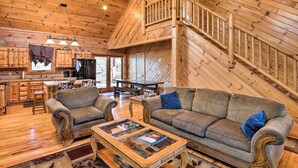 A spacious living room with a wooden staircase, a dining area, and a kitchen with wooden cabinets. - Bryson City Cabin w/ Private Hot Tub & Game Room (Bryson City)
