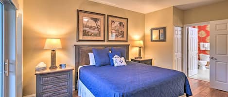 A bedroom with a large bed, two bedside tables with lamps, a ceiling fan, and framed pictures on the wall.