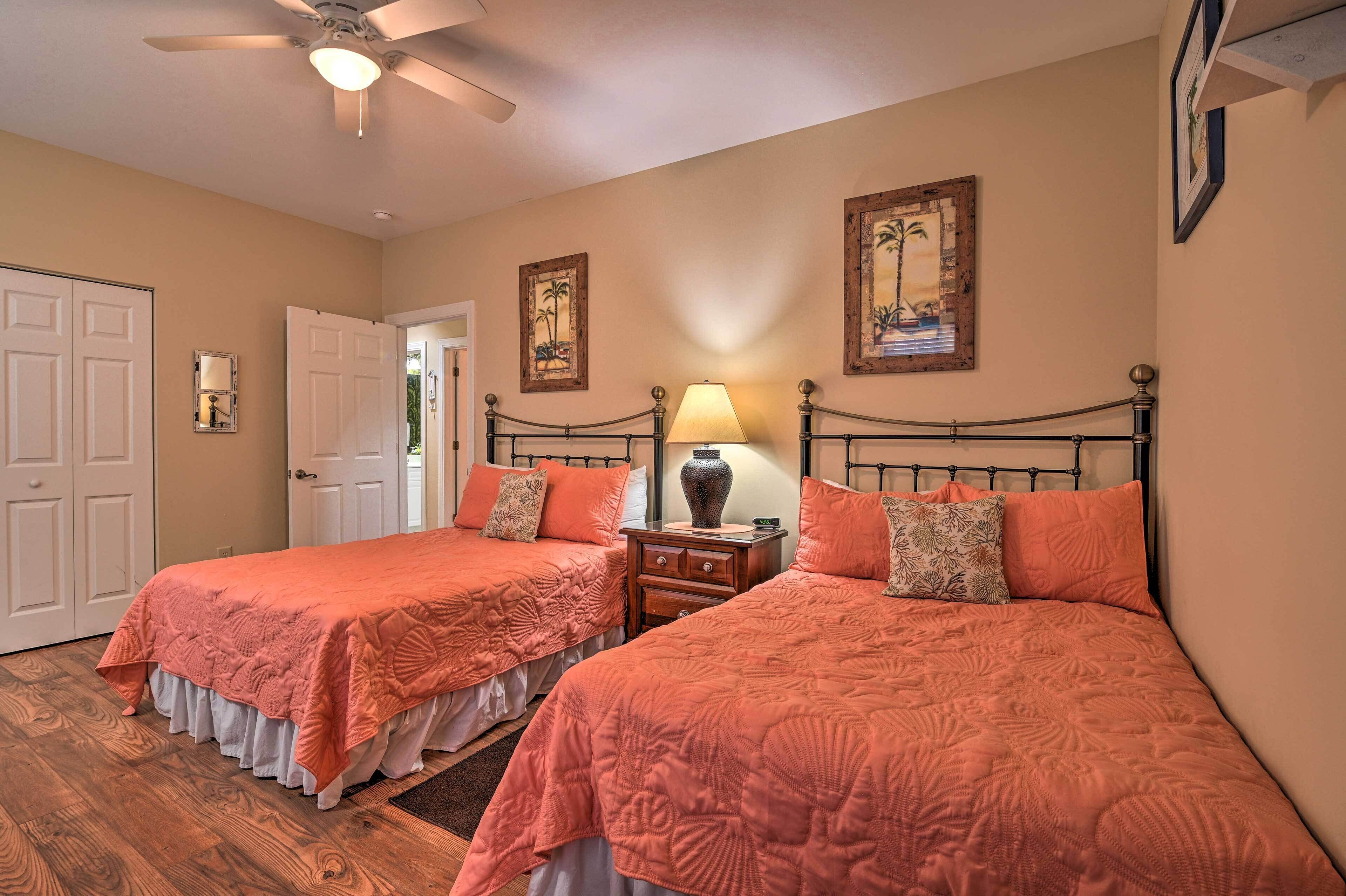 A bedroom with two beds, a ceiling fan, a nightstand with a lamp, and framed artwork on the walls.