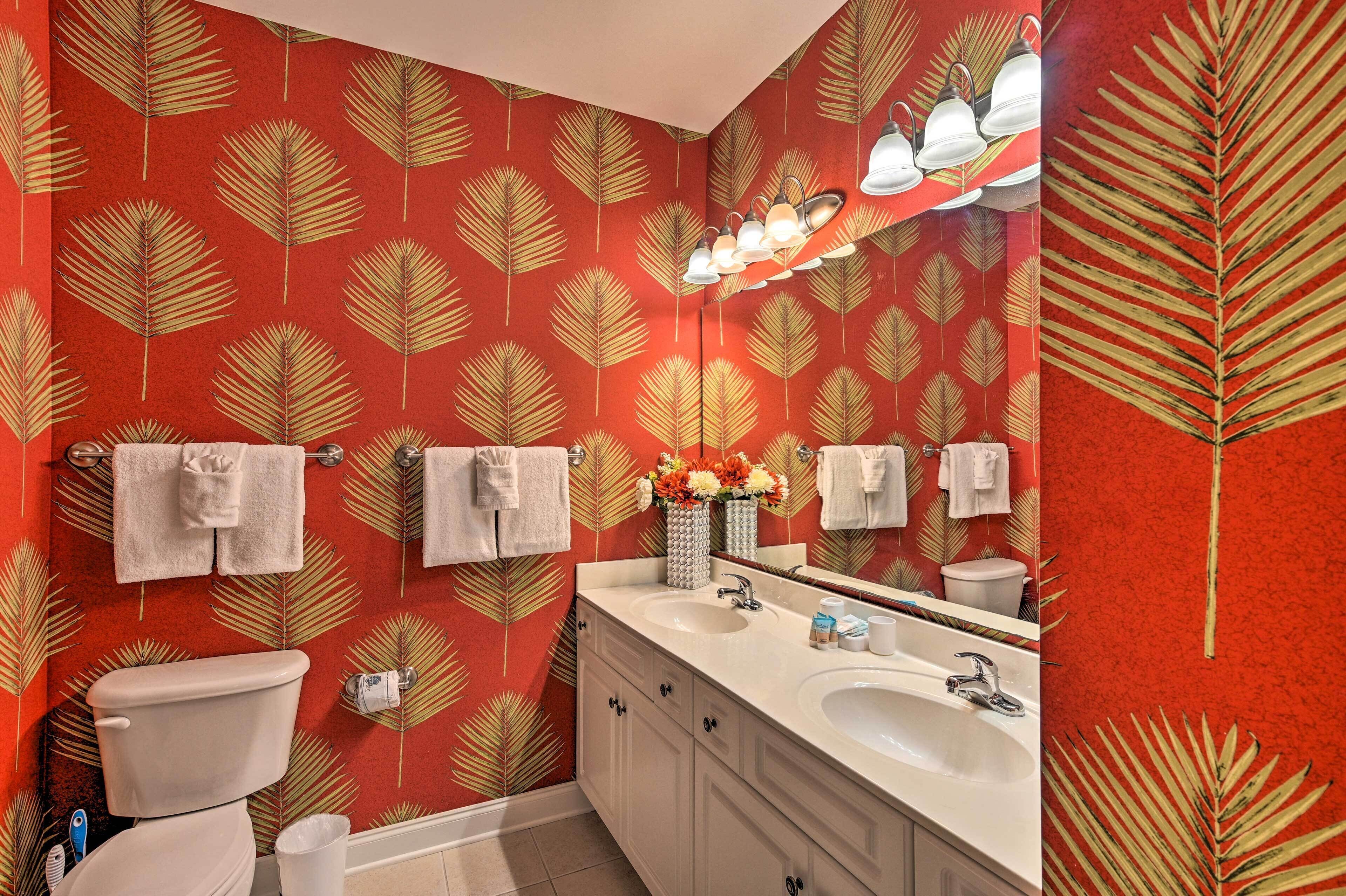 A bathroom with a red leaf-patterned wall, two sinks, a toilet, and a mirror with lights.