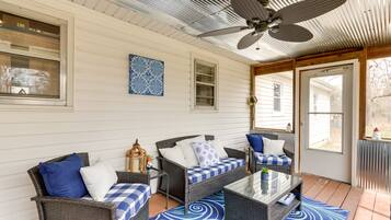 A covered porch with wicker furniture, a ceiling fan, and a blue patterned rug.
