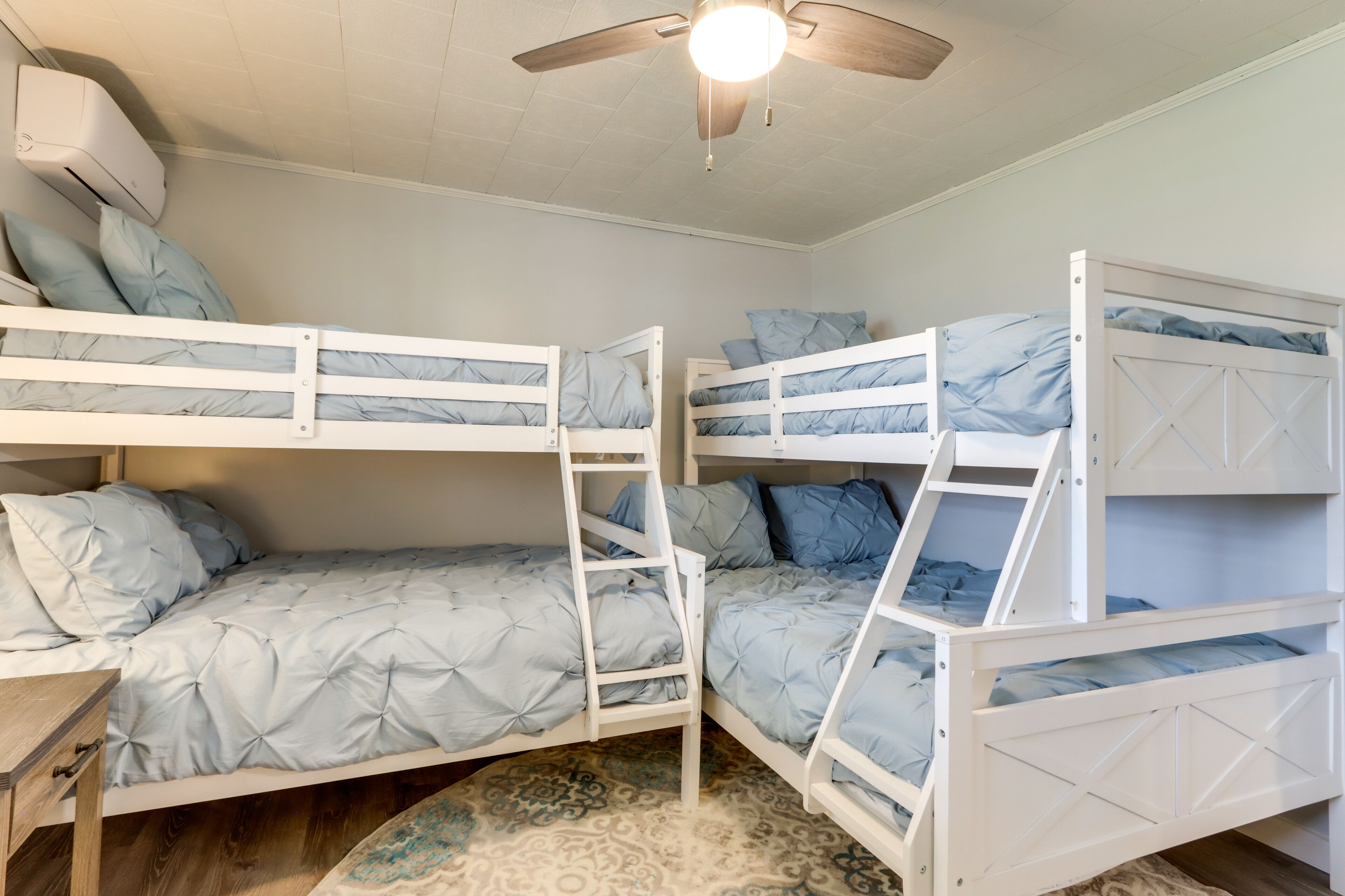 Une chambre avec un lit superposé, un ventilateur de plafond, un plancher en bois et un tapis à motifs.