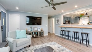 A modern living room with a sofa, a coffee table, a TV mounted on the wall, and a kitchen area with bar stools. - Pittsburg Vacation Rental < 1 Mi to Boat Launch (Pittsburg)