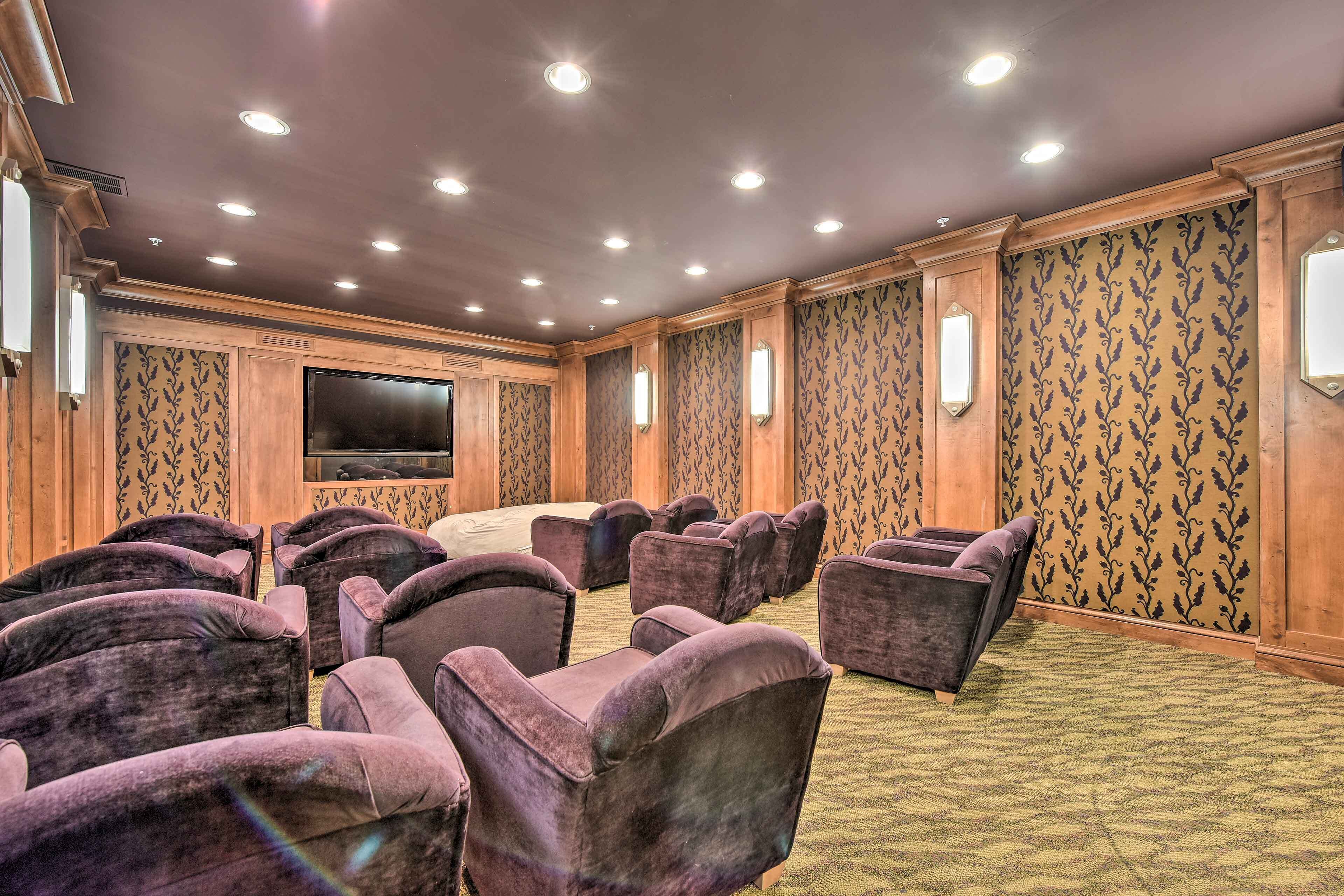 A theater room with rows of purple velvet chairs, a large screen, and patterned wallpaper.