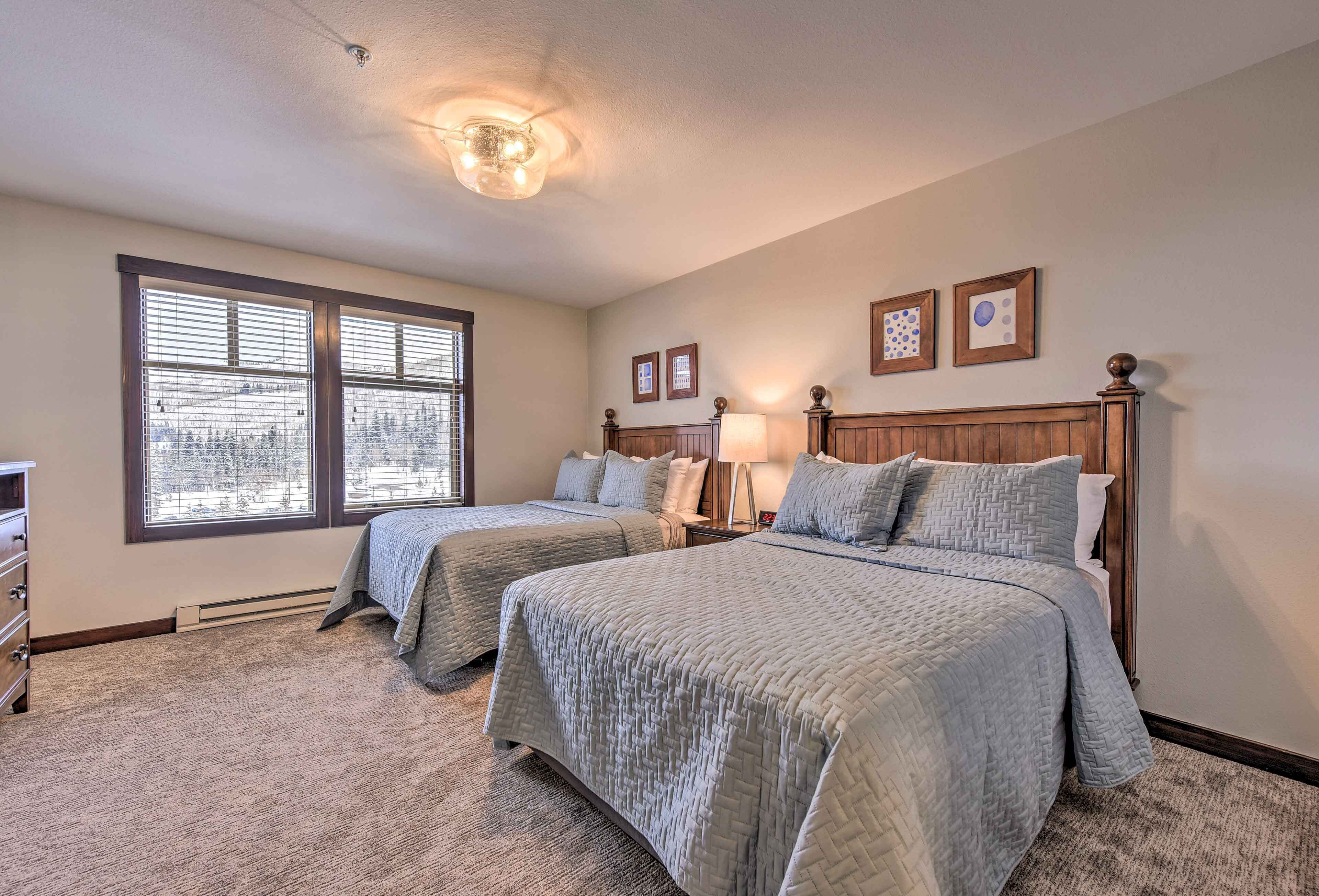 A bedroom with two beds, a dresser, a nightstand, and a window with blinds.