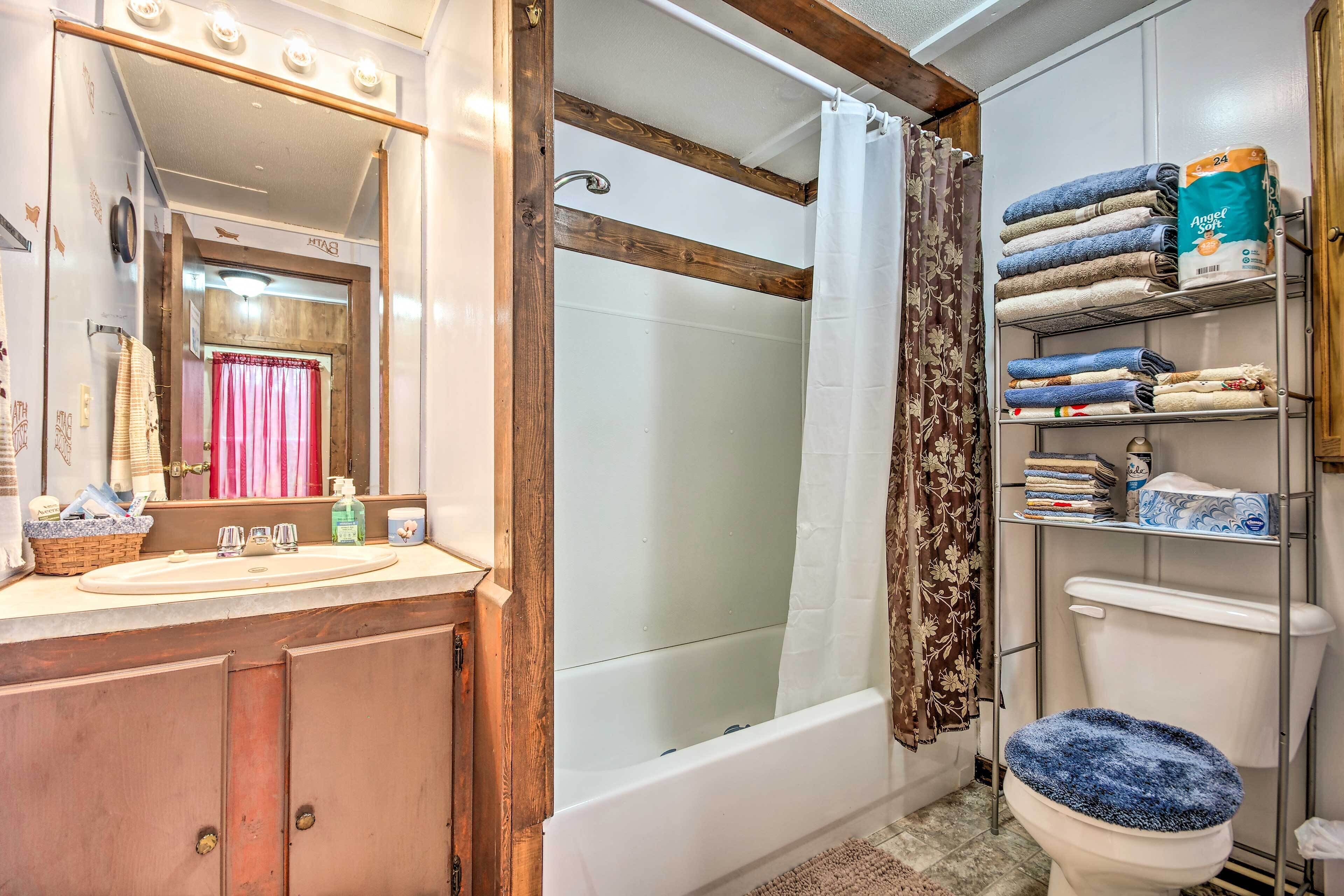 A bathroom with a wooden vanity, a bathtub, a toilet with a blue seat cover, and a shelf with towels and toiletries.