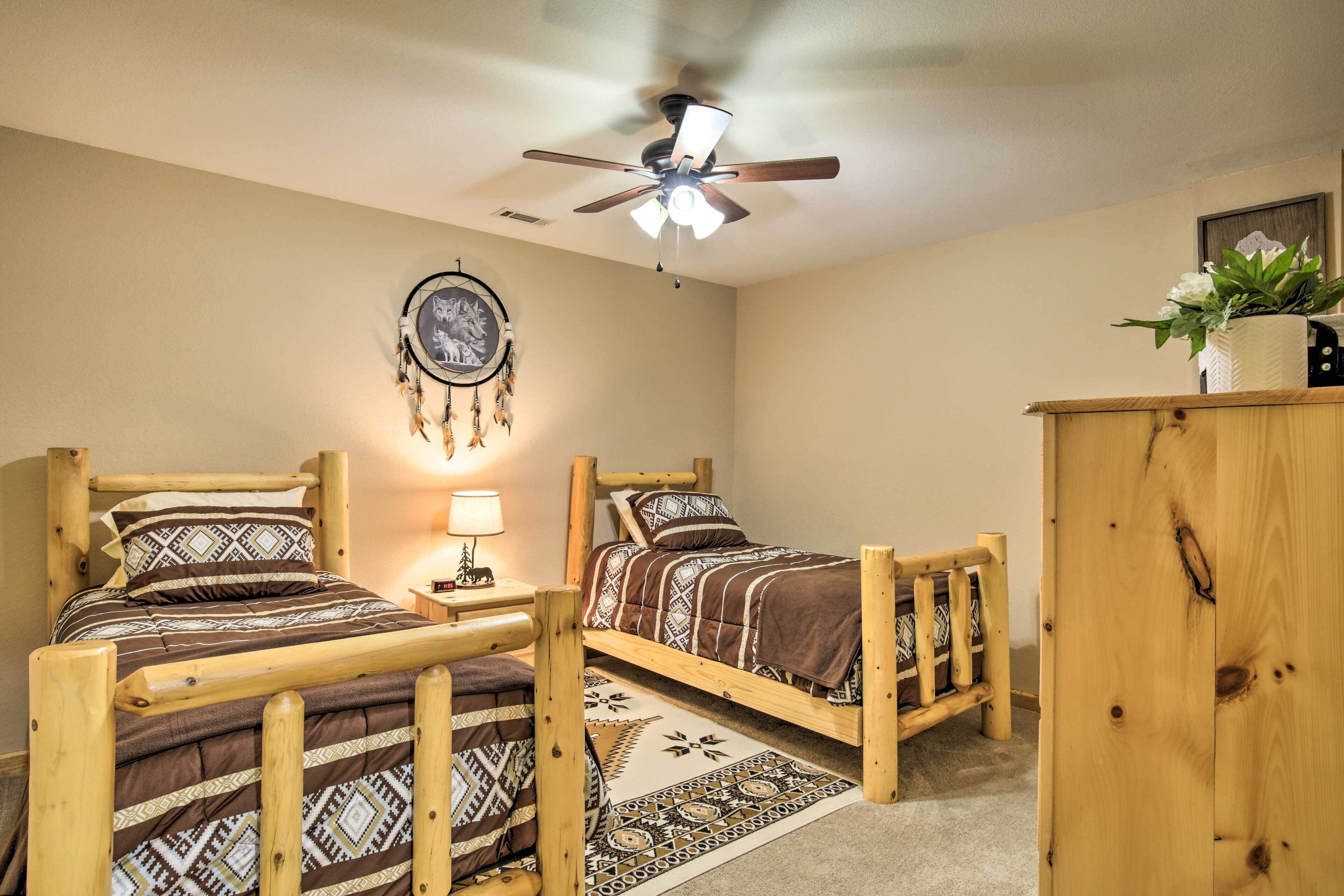Quarto com duas camas de madeira, um ventilador de teto, um sonho apanhador e uma planta sobre um armário.