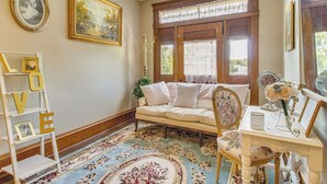 A cozy room with a floral-patterned rug, a sofa, a chair, and a small table with a vase of flowers. - Creekfront Yellville Manor w/ Parlors & Fire Pit! (Yellville)
