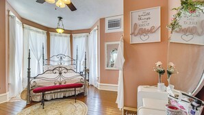 A bedroom with a four-poster bed, a round rug, a vanity with toiletries, and decorative wall art. - Creekfront Yellville Manor w/ Parlors & Fire Pit! (Yellville)