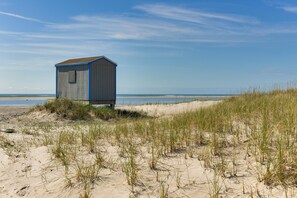A beach hut with a simple structure, situated on a sandy dune with grass in the foreground. - Brigantine Condo w/ Beach Access & Pool Views (Brigantine)