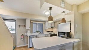 A modern kitchen with a central island, pendant lights, and a microwave. - Brigantine Condo w/ Beach Access & Pool Views (Brigantine)