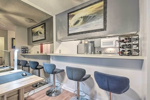 Un'area bar moderna con sgabelli grigi, un bancone bianco e una cantinetta per vini.
