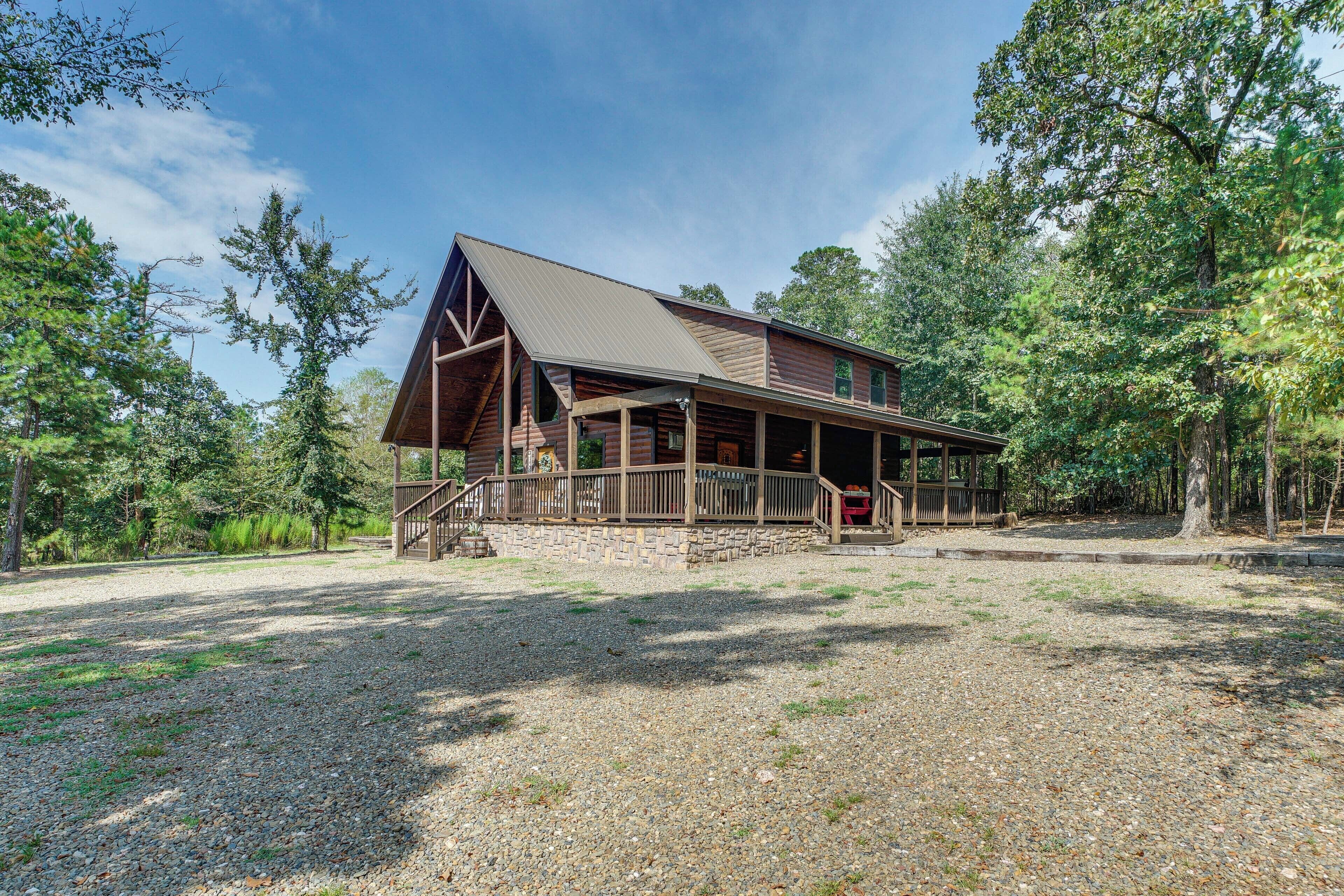 Un chalet rustique doté d’une véranda, entouré d’arbres et d’un sol en gravier.