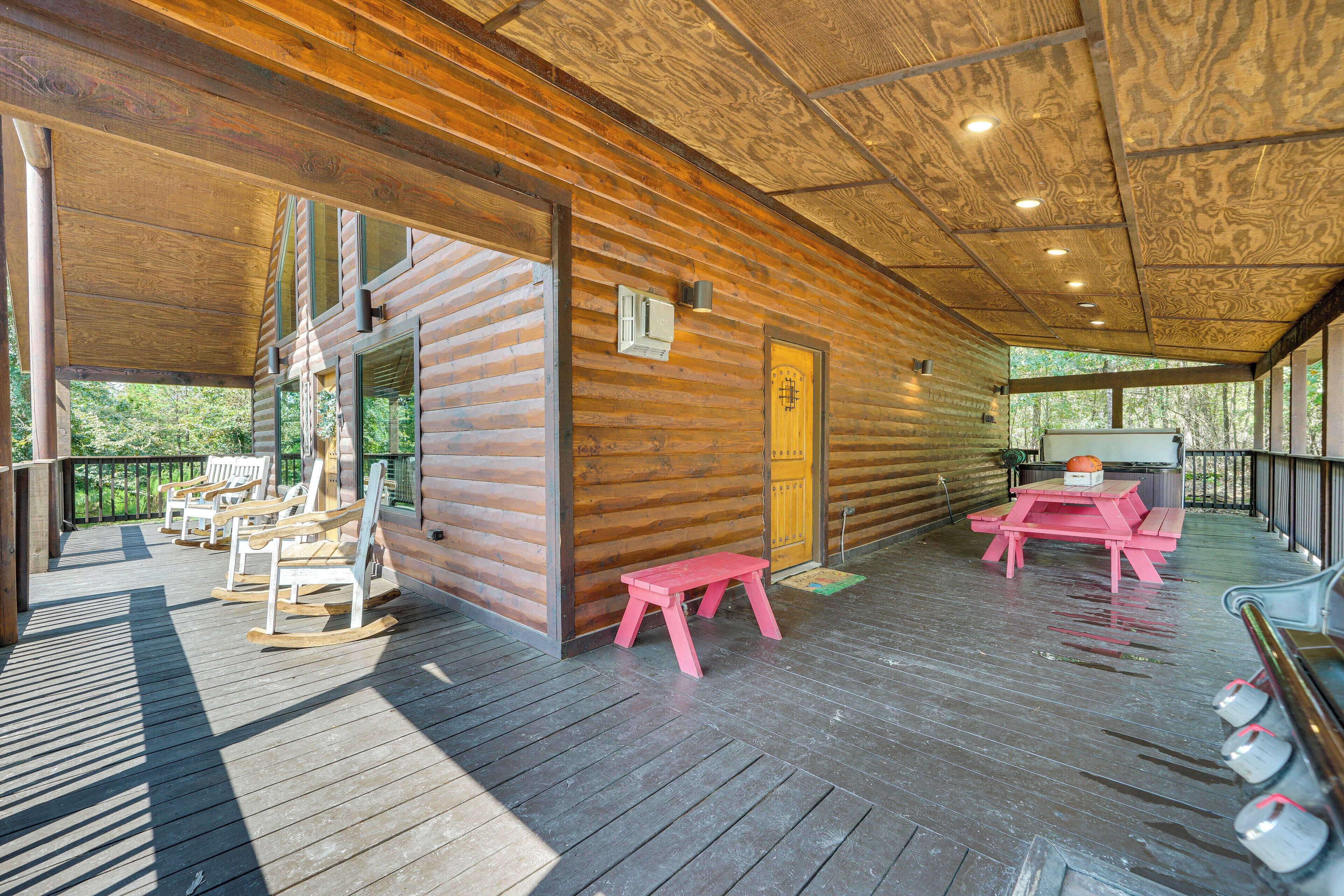 Uma cabana de madeira com varanda, cadeiras de balanço, um banco rosa e uma mesa de piquenique.
