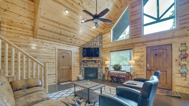 A log cabin interior with a fireplace, leather sofa, dining area, and a staircase. - 'penny Lane Lodge' Broken Bow Cabin < 6 Mi to Lake (Broken Bow)