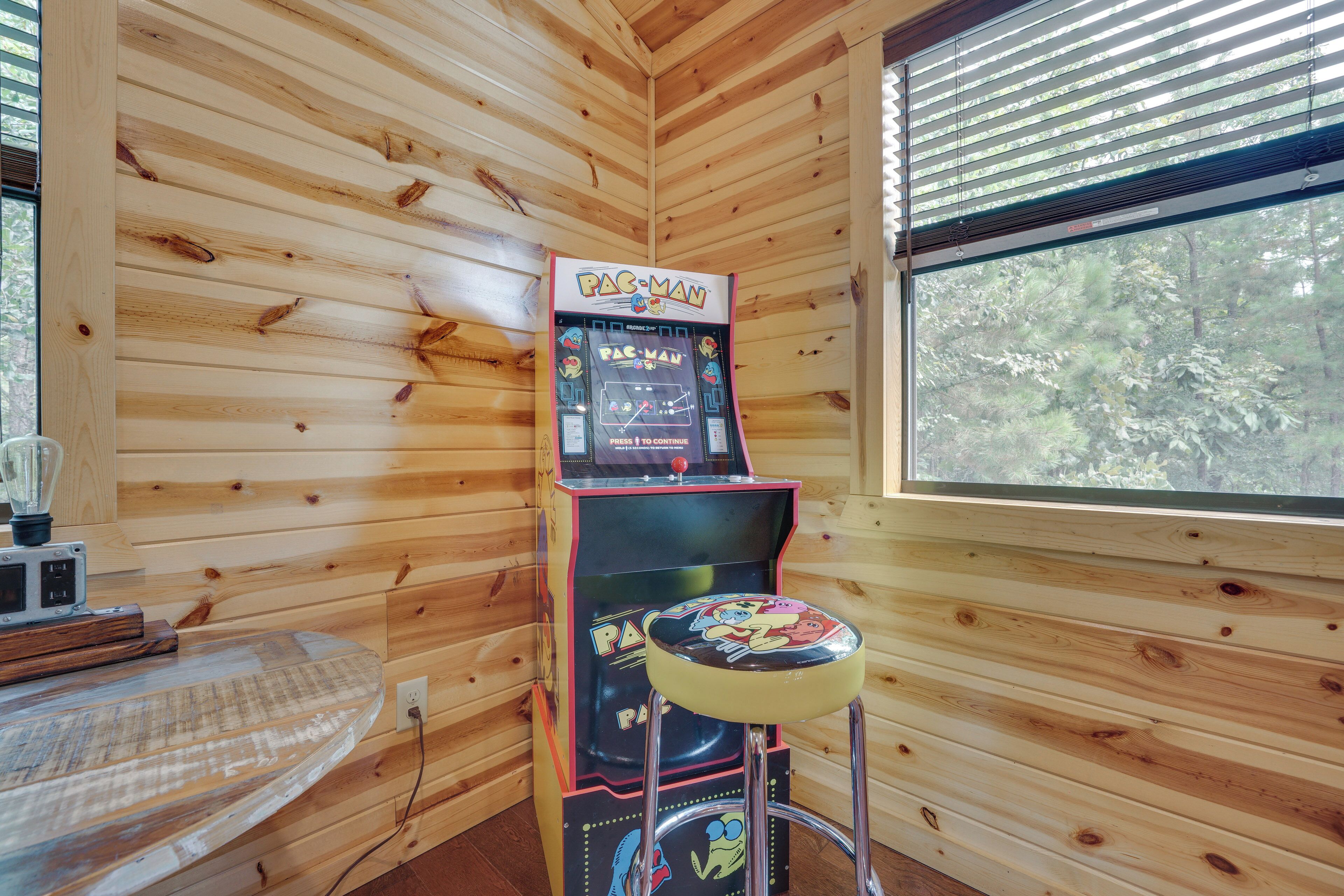 A Pac-Man arcade machine in a wooden cabin with a window.