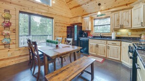 A wooden cabin interior with a dining table, chairs, a bench, a refrigerator, a stove, and a window with blinds. - 'penny Lane Lodge' Broken Bow Cabin < 6 Mi to Lake (Broken Bow)