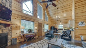 A spacious log cabin interior with a fireplace, dining area, kitchen, and a large window providing natural light. - 'penny Lane Lodge' Broken Bow Cabin < 6 Mi to Lake (Broken Bow)