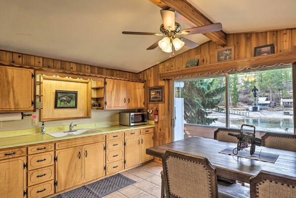 A wooden kitchen with a large window, a ceiling fan, and a dining area with a table and chairs.