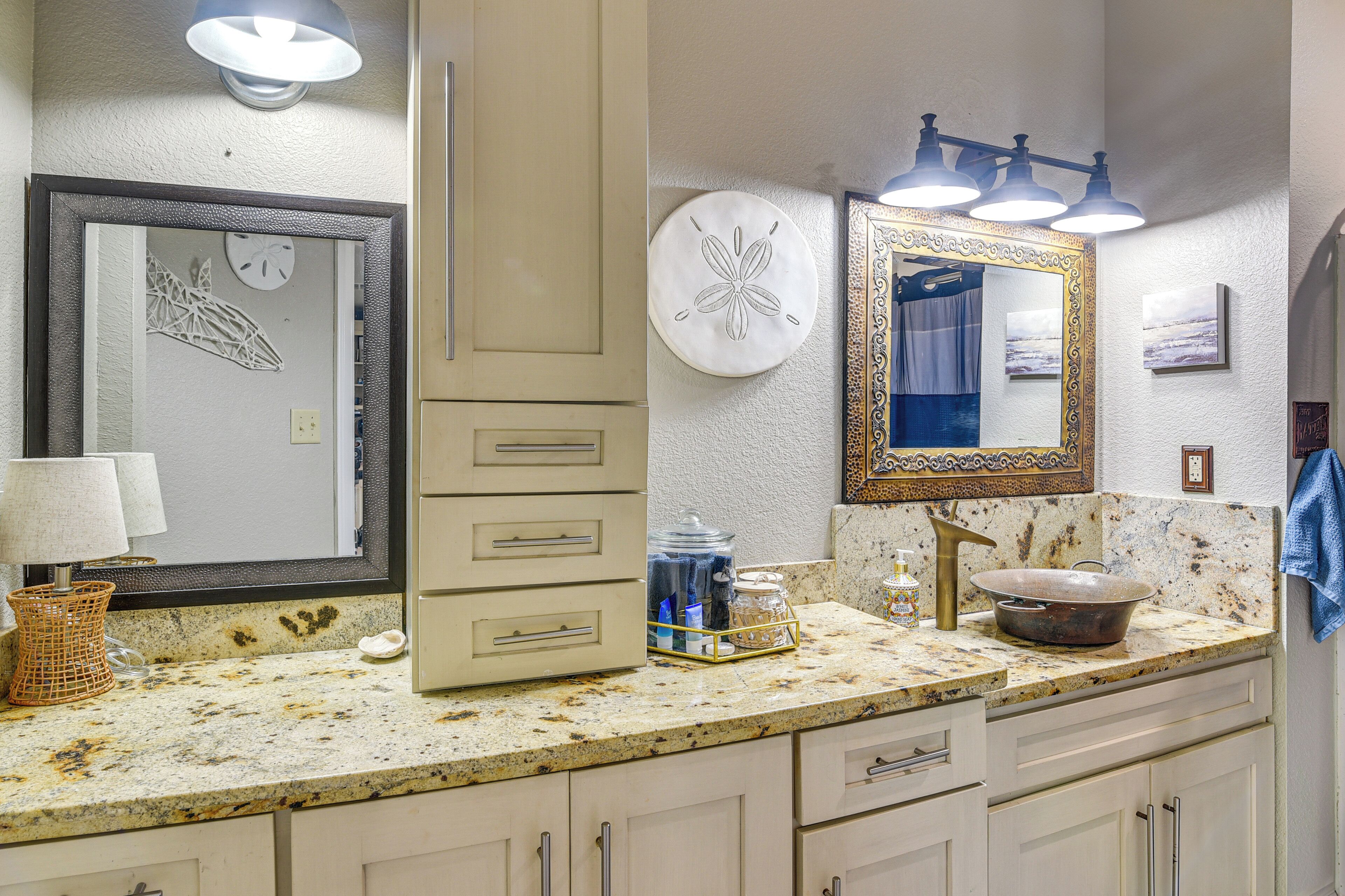A bathroom with a granite countertop, a sink with a vessel basin, a mirror with a decorative frame, and a wall clock.