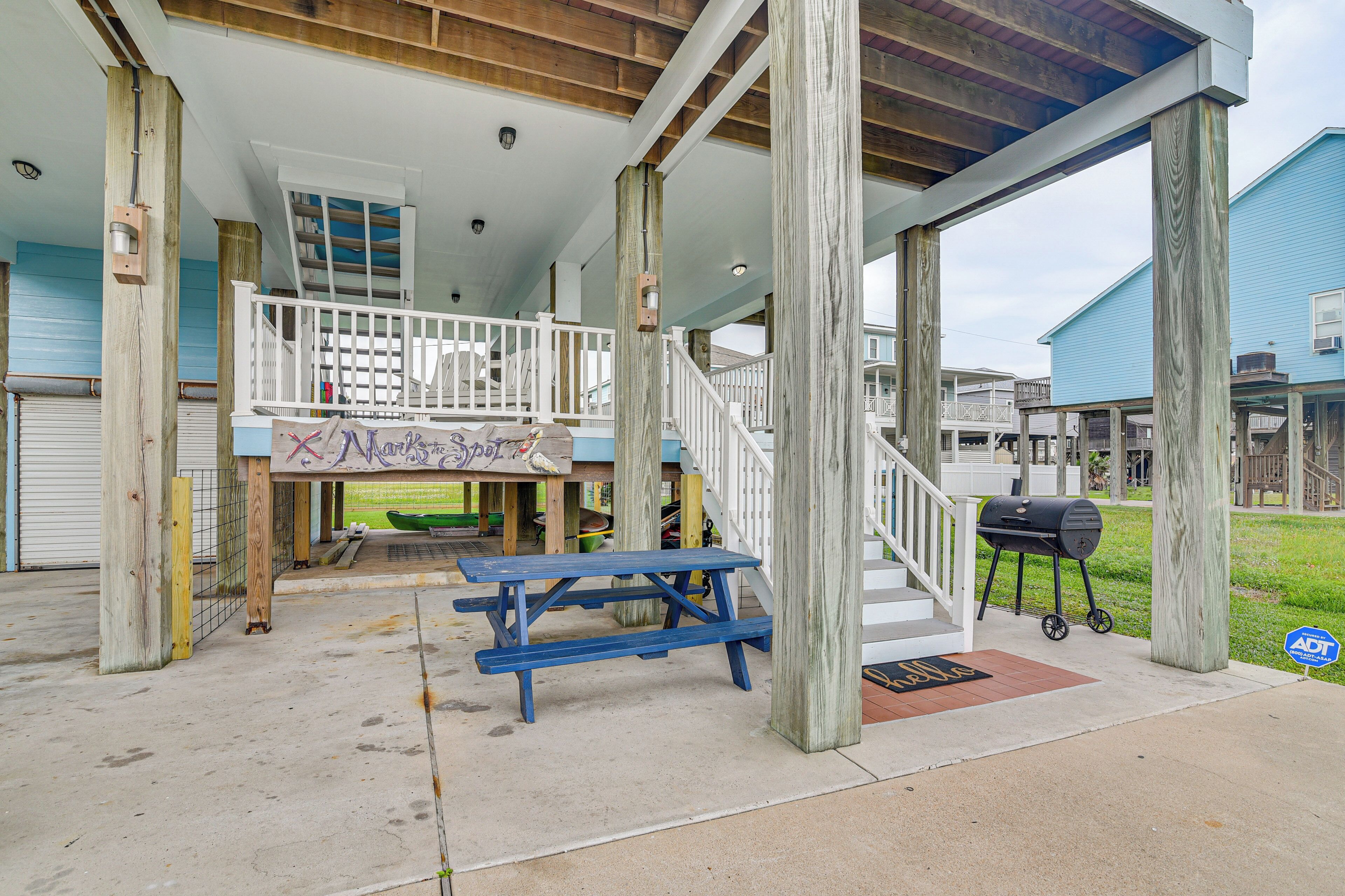A covered outdoor area with a picnic table, a barbecue grill, and a staircase leading to a second level.