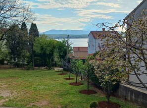 A residential area with a grassy yard, trees, and a building with a red roof. - Holiday apartment close to the sea (Malinska)