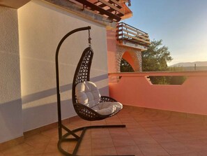A hanging chair with a cushioned seat and back, attached to a metal stand, positioned on a tiled patio area.