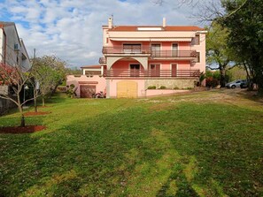 Une maison à deux étages avec un toit recouvert de tuiles rouges, un jardin devant et une voiture garée.