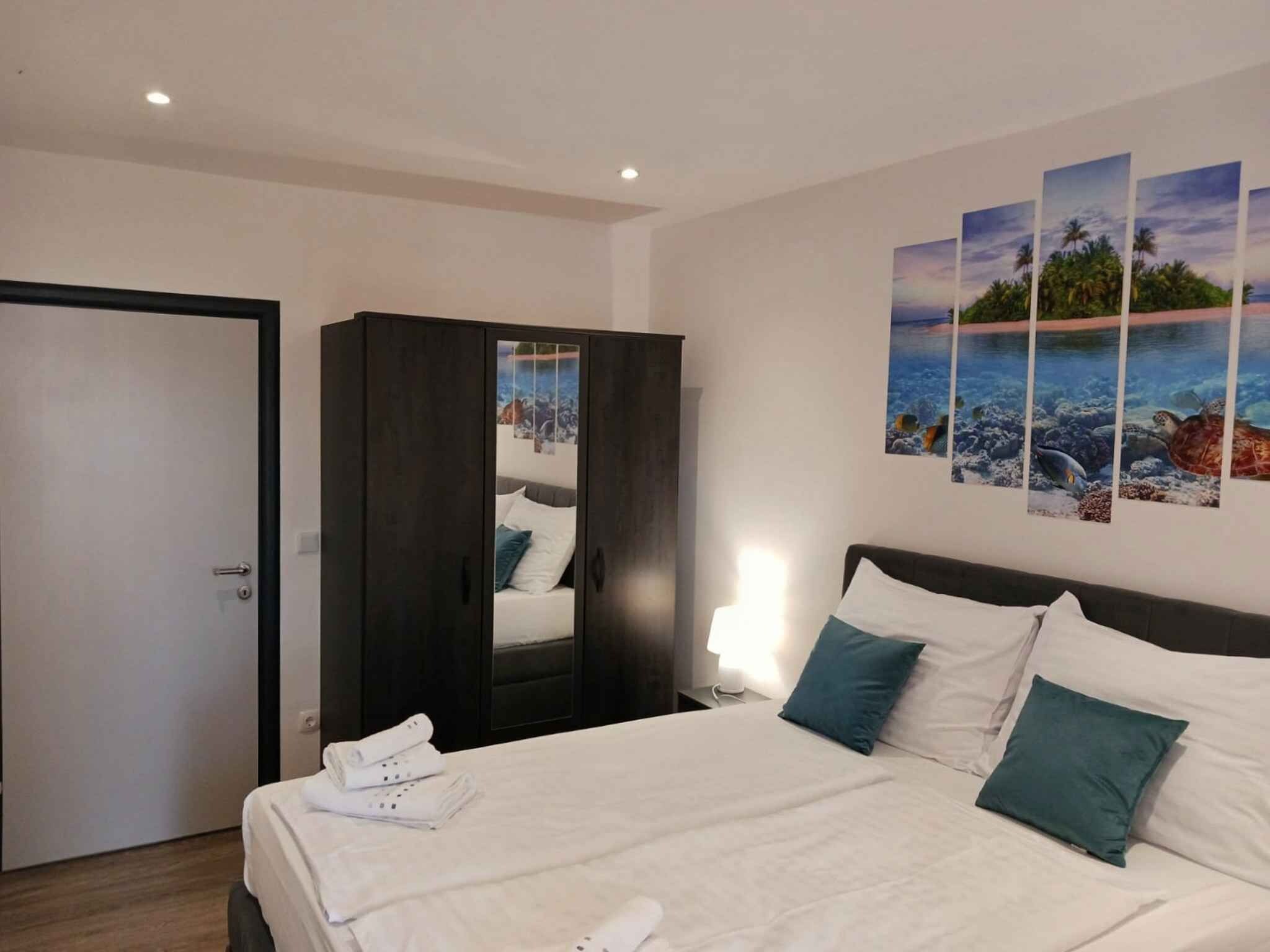 A hotel room with a bed, a wardrobe, a door, and a wall with a tropical mural.