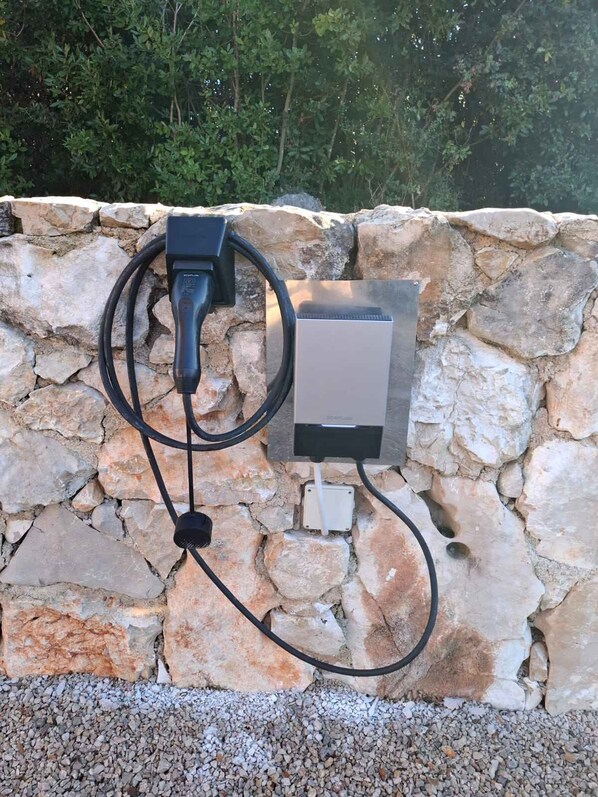 A stone wall with a power outlet and a black electrical cord plugged in.
