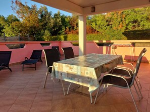 Une terrasse extérieure avec une table et des chaises, entourée d’un mur rose et offrant une vue sur les arbres.
