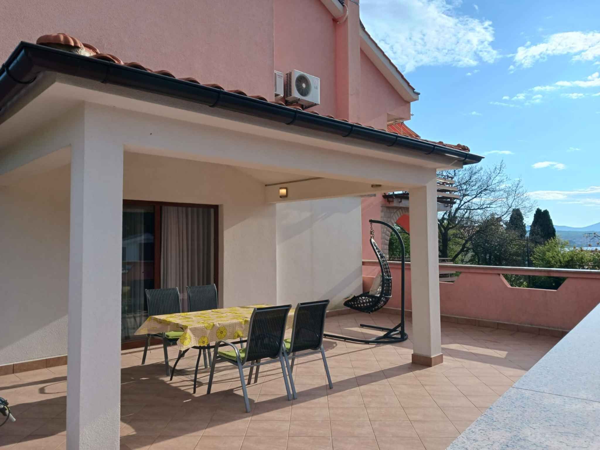 Un patio techado al aire libre con una mesa y sillas, una silla con respaldo, y vistas al cielo y al paisaje lejano.