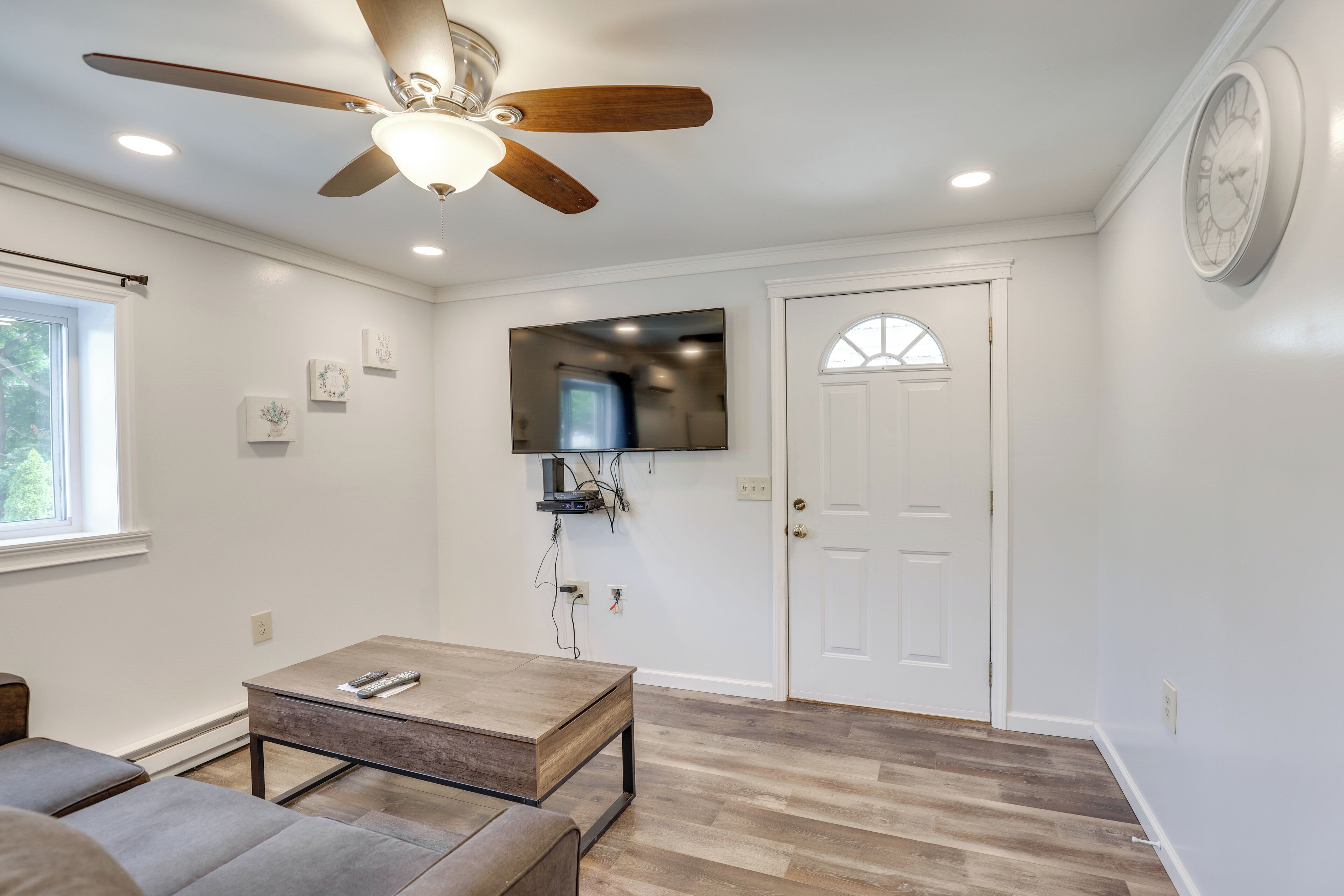 A living room with a ceiling fan, a flat-screen TV mounted on the wall, a wooden coffee table, and a door with a window.