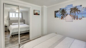 Une chambre avec un lit, une porte-fenêtre coulissante donnant sur une salle de bain, et un mur orné de trois tableaux représentant des palmiers.