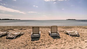 A beach with four lounge chairs facing the ocean, a clear sky, and a distant shoreline.
