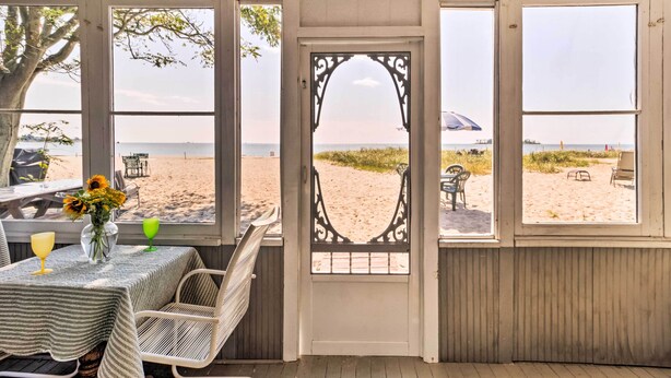 A beachside room with a view of the beach, a table with a vase of flowers, and a chair.
