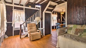 A cozy room with a wooden floor, a sofa, a chair, a lamp, and a staircase.