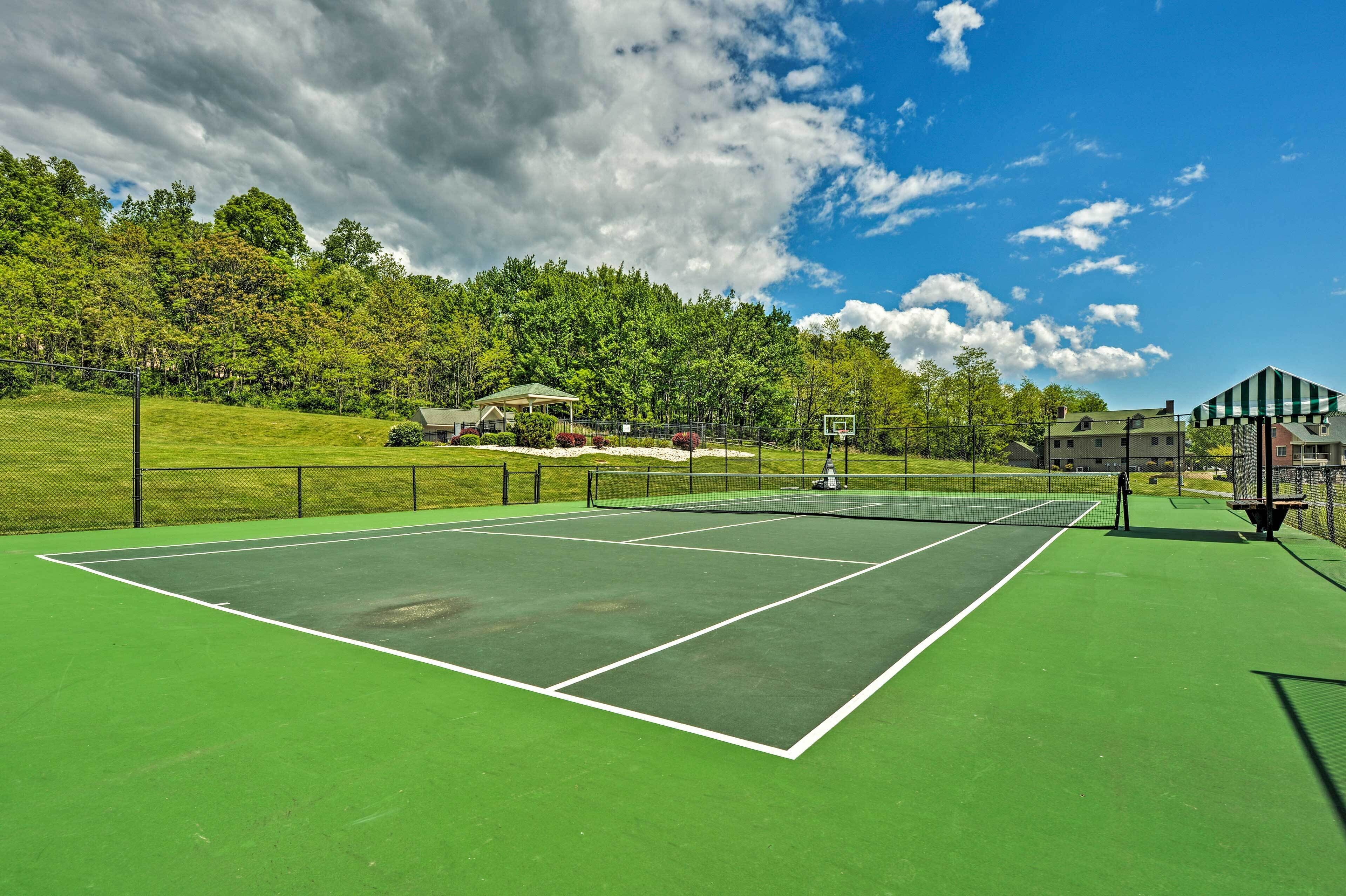 Ein Tennisplatz mit grüner Belag, umgeben von einem Zaun, und ein kleines Pavillon im Hintergrund.
