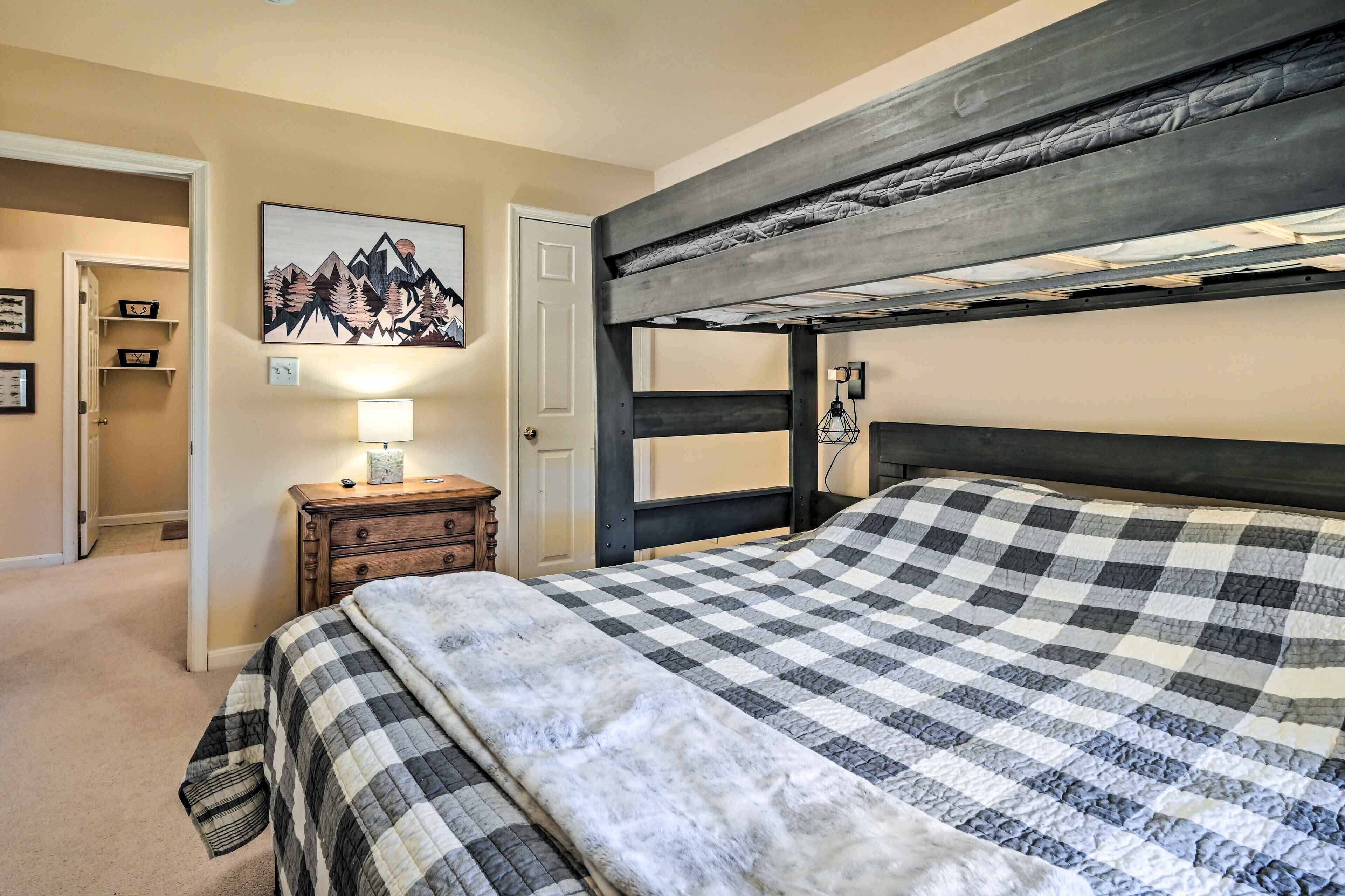 A bedroom with a bunk bed, a checkered bedspread, a bedside lamp, and a mountain painting on the wall.