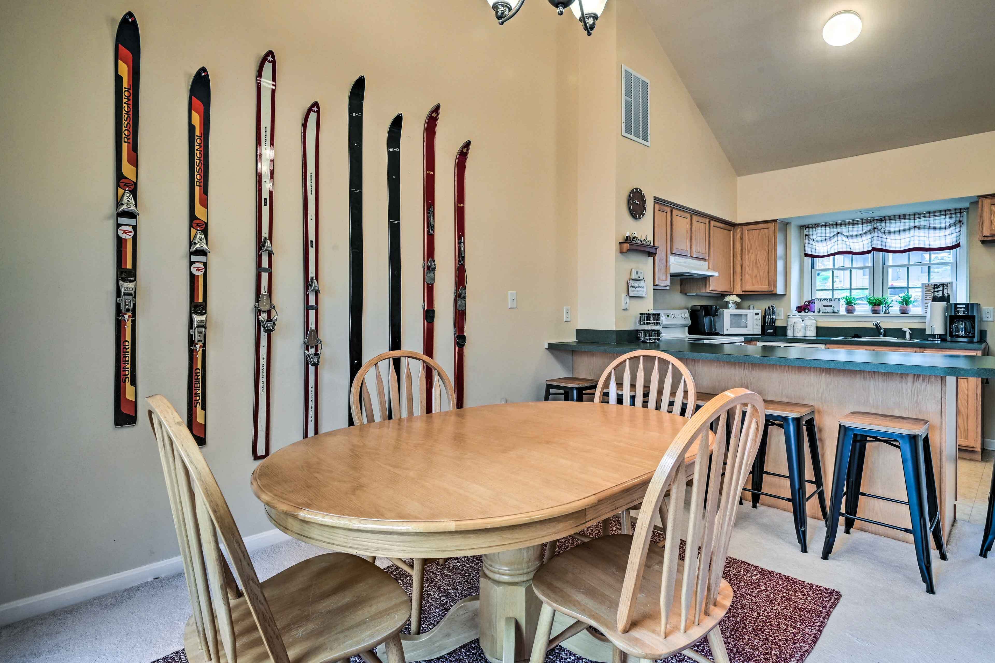 A dining area with a round table and chairs, a kitchen with modern appliances, and a row of skis on the wall.