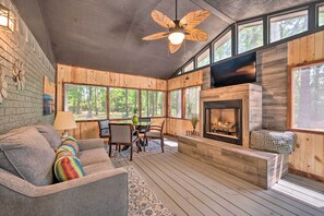 A cozy cabin interior with a fireplace, wooden walls, and large windows. - Lavish Broken Bow Home on 6 Acres w/ Hot Tub! (Broken Bow)