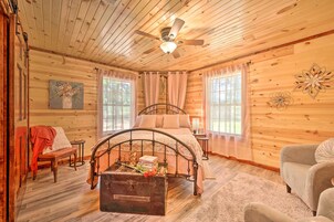 Un dormitorio de cabaña de madera con una cama, un banco, una maleta y un ventilador de techo.