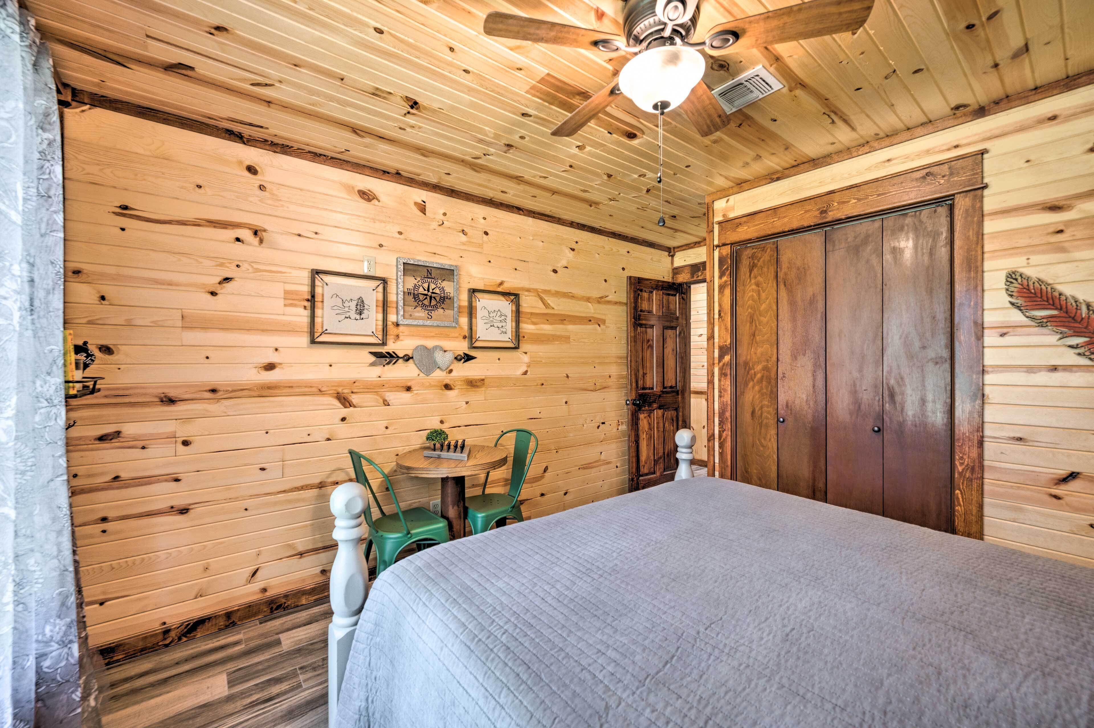 A wooden cabin room with a bed, a ceiling fan, and a wooden door.