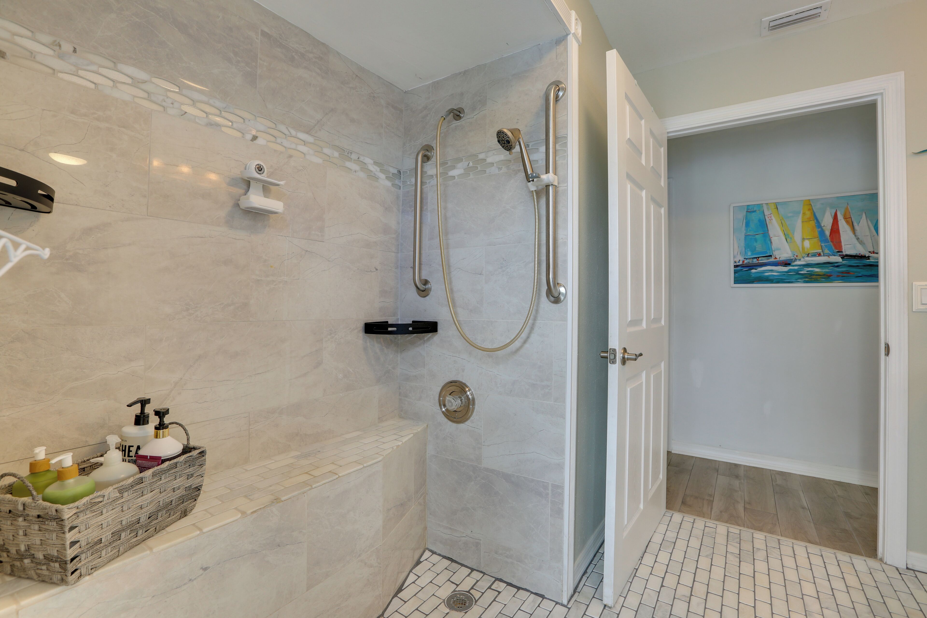 A bathroom with a walk-in shower, a bench, and a basket of toiletries.
