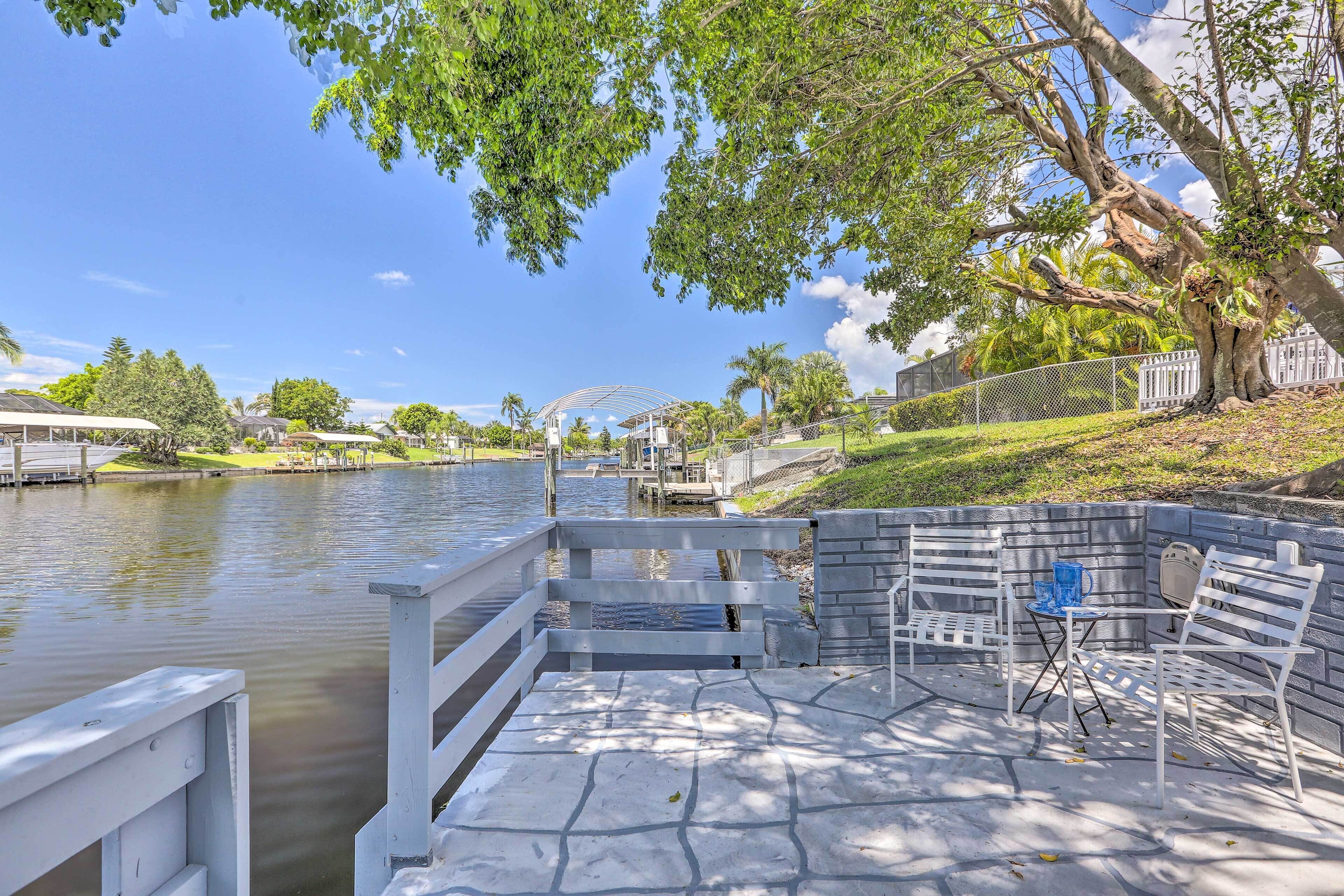 A waterfront patio with a stone deck, white railings, and outdoor seating.