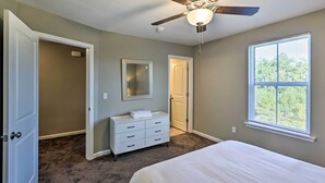 Ein Schlafzimmer mit Bett, Kommode, Deckenventilator und Fenster.