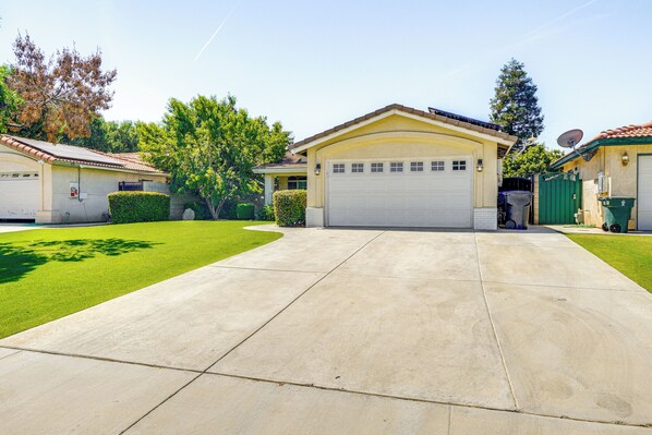 A residential driveway leading to a garage with a satellite dish and a green trash bin.