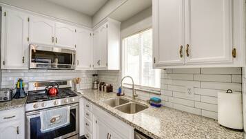 A kitchen with white cabinets, a stainless steel stove, a double sink, and a window with blinds.