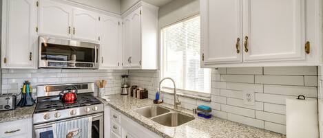 A kitchen with white cabinets, a stainless steel stove, a double sink, and a window with blinds.